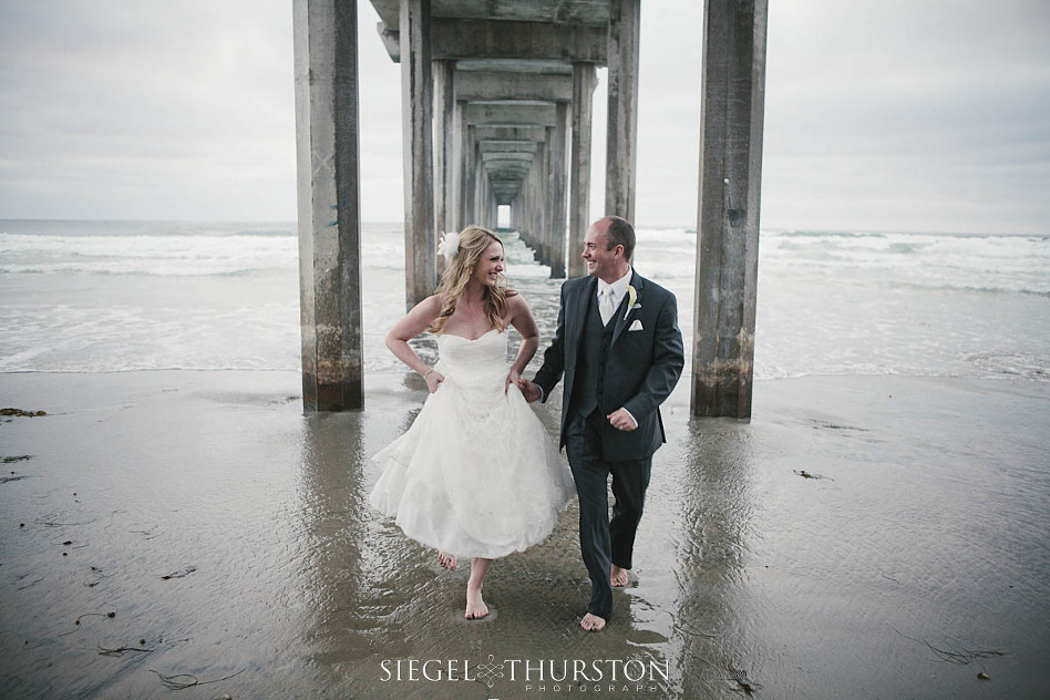 bride and groom having fun under the scripps pier