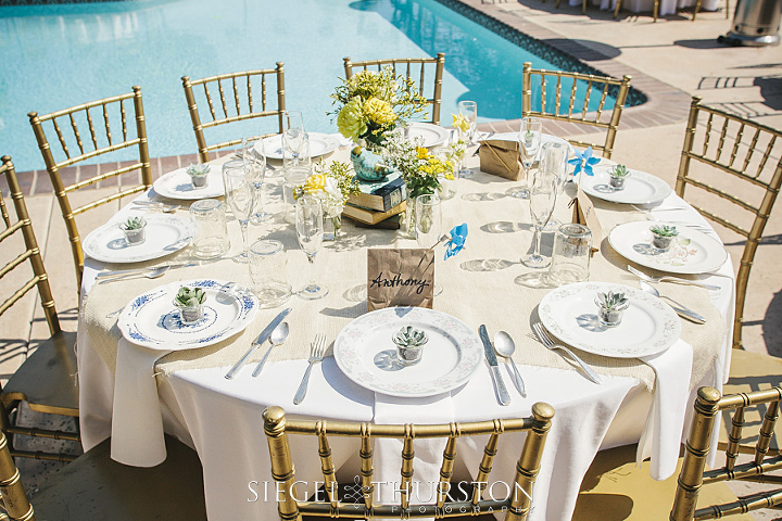 round wedding tables with center piece consisting of mason jars, books, ceramic birds, yellow and white flowers