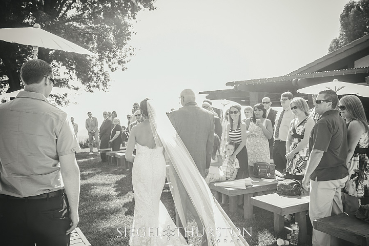 bride wearing a cathedral lenght veil walking down the aisle with her father