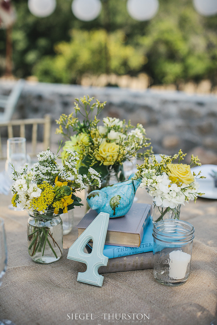 center piece consisting of mason jars, books, ceramic birds, yellow and white flowers