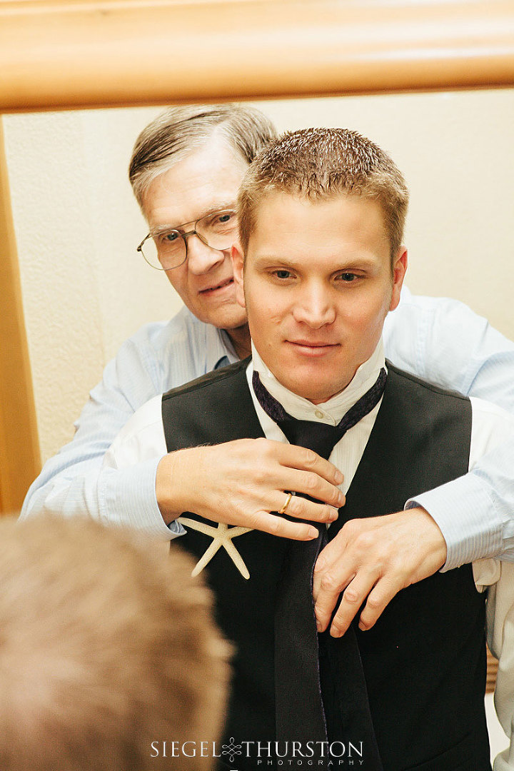 father of the groom helping his son tie his tie for the wedding day
