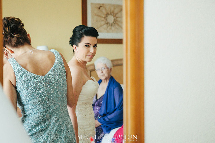 grandmother watching her granddaughter get into her wedding dress from the mirror
