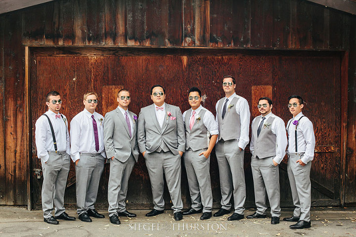 Fun groomsmen portraits. All the groomsmen are wearing different variations of gray suits. Some have vests on while others have ties or suspenders.