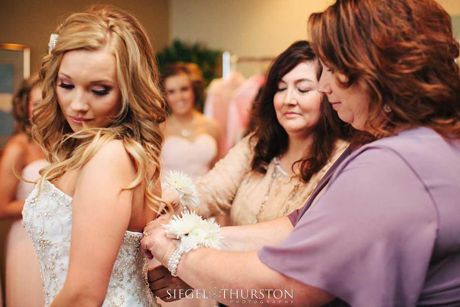 mom and stepmom helping the bride into her wedding dress