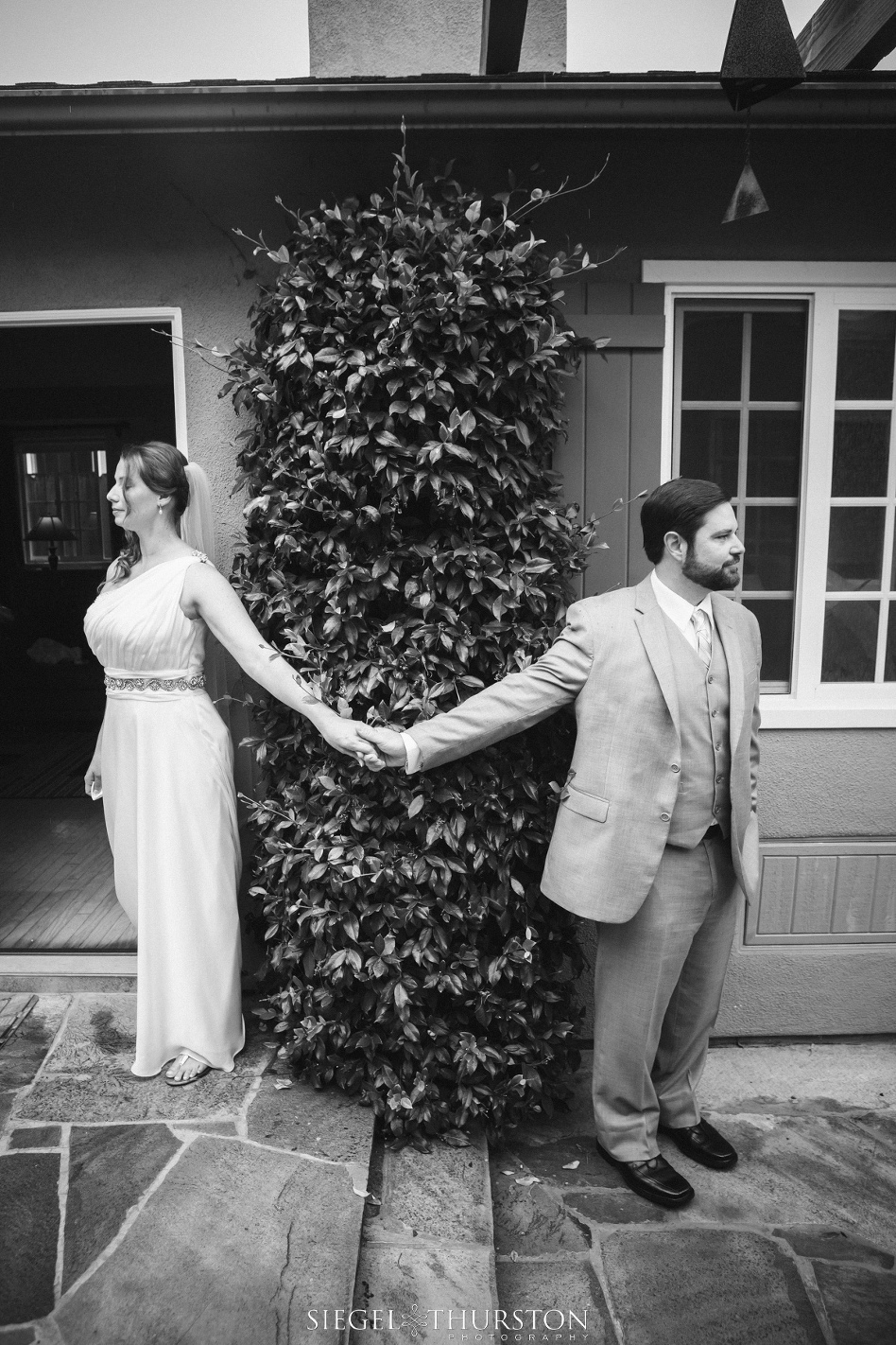 Bride and groom holding hands around a corner before their wedding ceremony but not seeing one another