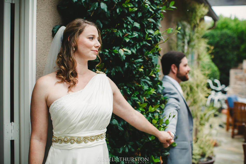 Bride and groom holding hands around a corner before their wedding ceremony but not seeing one another