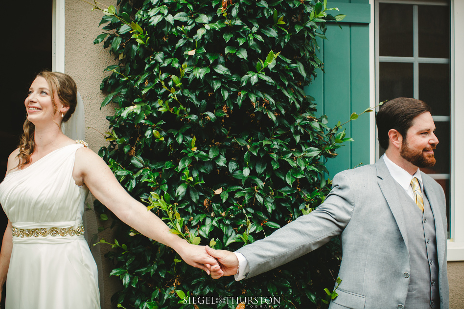 Bride and groom holding hands around a corner before their wedding ceremony but not seeing one another