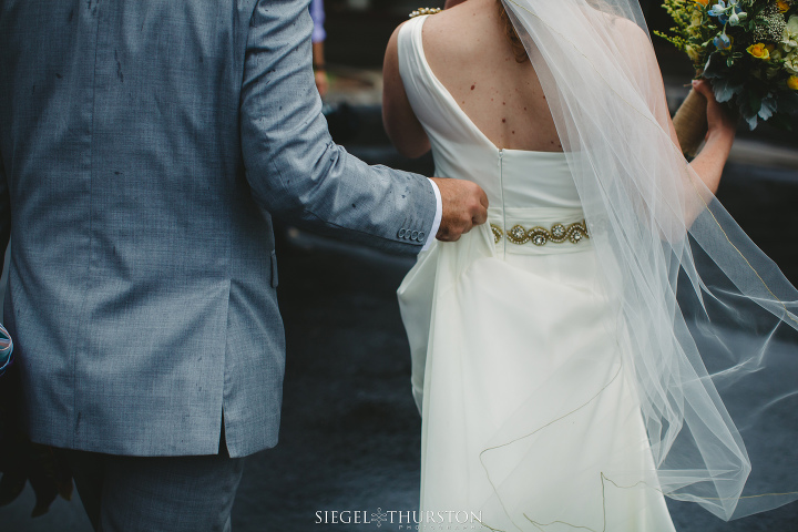 romantic moment of the groom holding the brides wedding dress as they walk