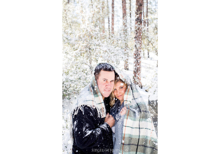 romantic snowing engagement photos with the couple wrapped in a plaid blanket